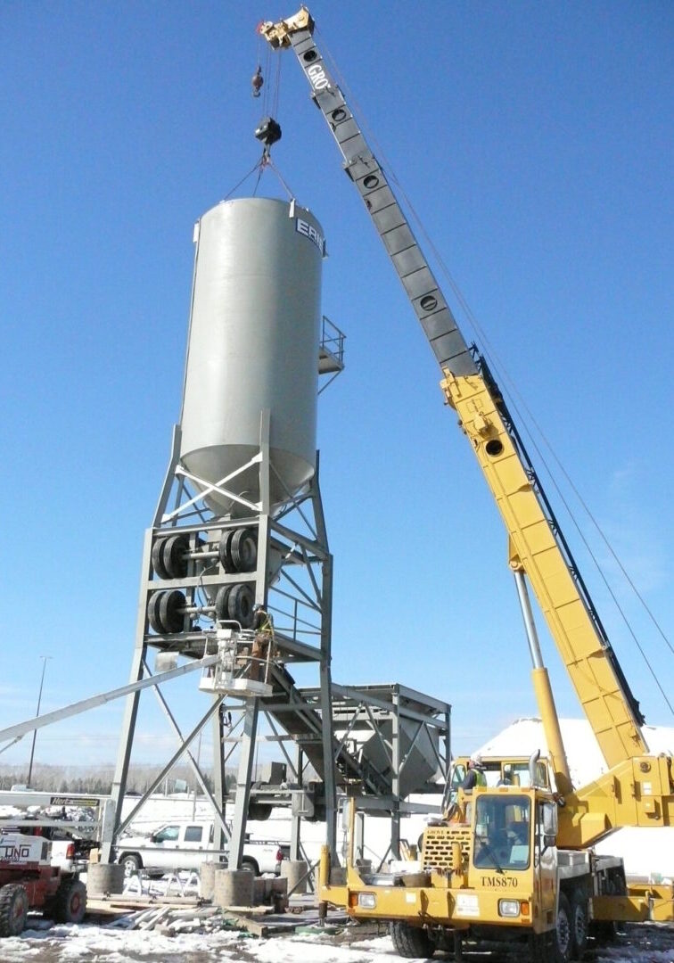A crane is lifting a cement mixer into place.